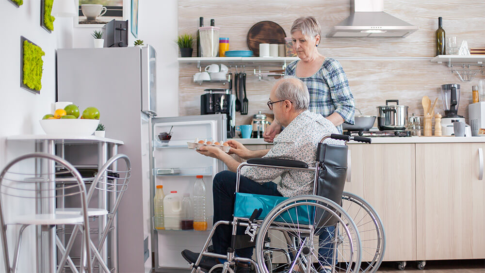 Một người cao tuổi ngồi xe lăn tự mở tủ lạnh và lấy đồ ra.